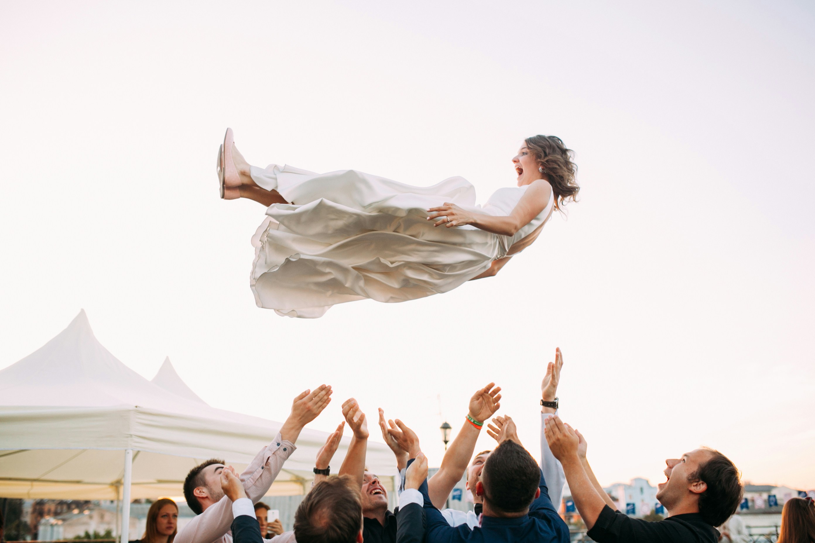 Une mariée en robe blanche qu'on fait sauter en l'air par ses invités lors de son mariage